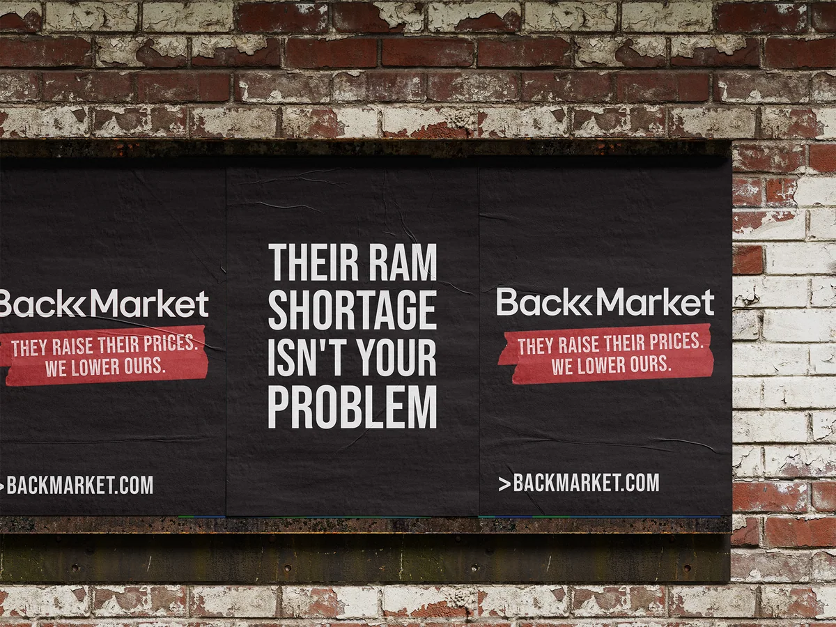 Posters pasted on a brick wall: “Their RAM shortage isn’t your problem” between two Back Market posters reading “They raise their prices. We lower ours.”