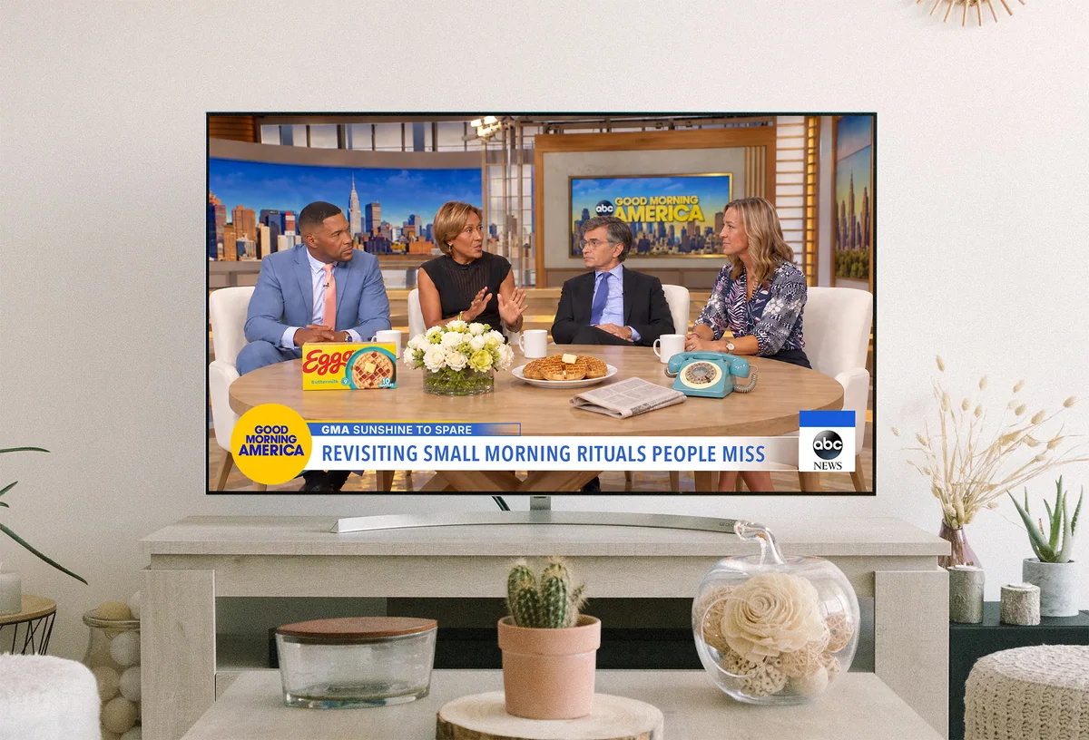 A living-room TV showing a morning-show panel around a table of Eggo waffles, captioned “Revisiting small morning rituals people miss”